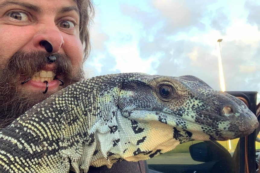 A bearded man holds up his pet lace monitor