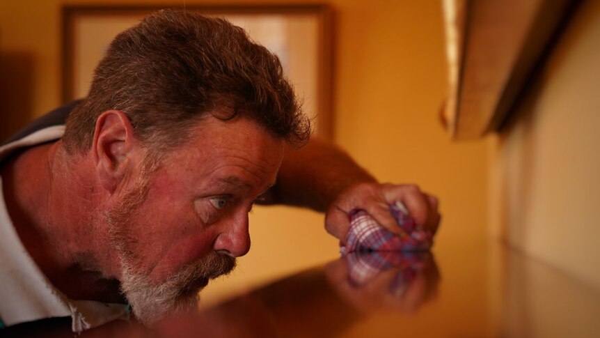 A close-up of a man polishing a wooden mantelpiece.