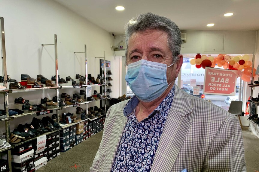 A man wearing a suit and a face mask stands in a shoe store.