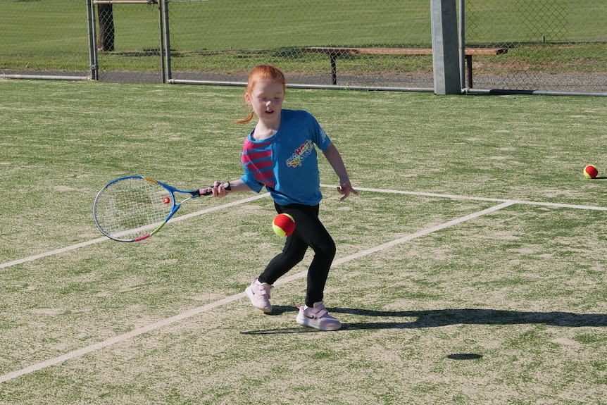 A girl wearing a blue shirt hitting a tennis ball 