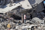 Four people look on in disbelief at the remains of their home, which is now concrete rubble, following an airstrike