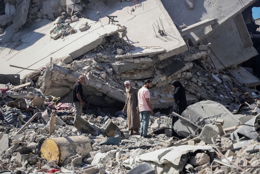 Four people look on in disbelief at the remains of their home, which is now concrete rubble, following an airstrike