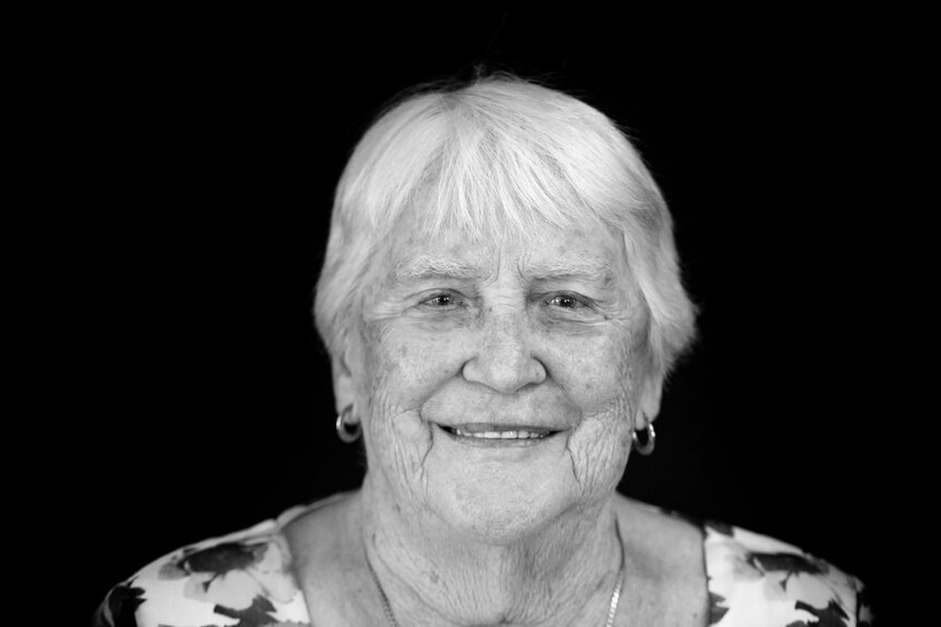 A black and white photo of an older woman with short white hair, earrings, smiling.