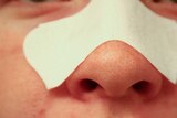 A person is seen wearing a blackhead strip with pores visible on their nose.