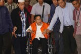 Setya Novanto sits on a wheelchair surrounded by standing men.