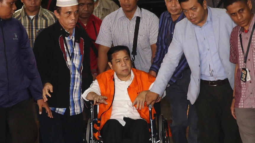 Setya Novanto sits on a wheelchair surrounded by standing men.