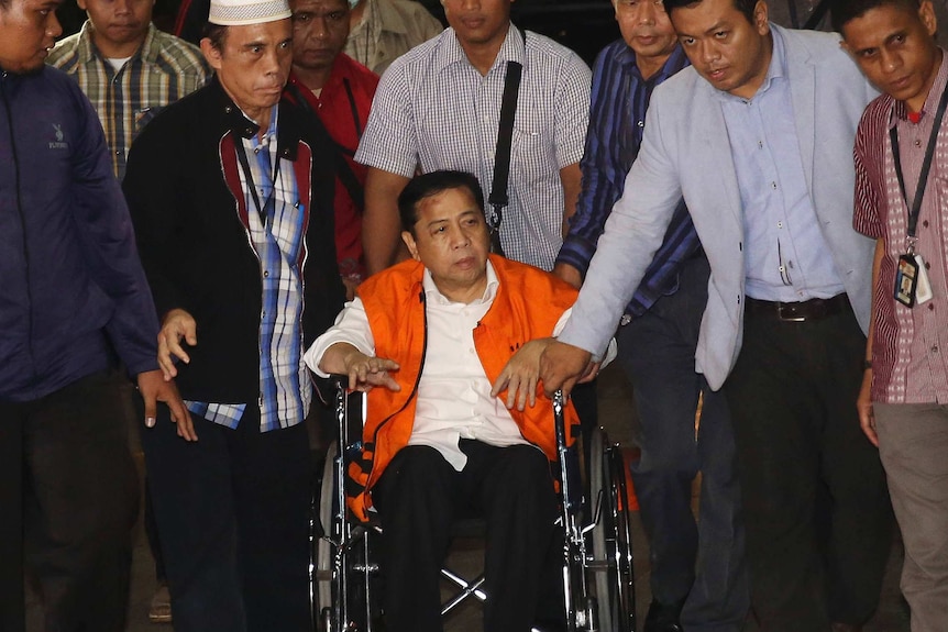 Setya Novanto sits on a wheelchair surrounded by standing men.