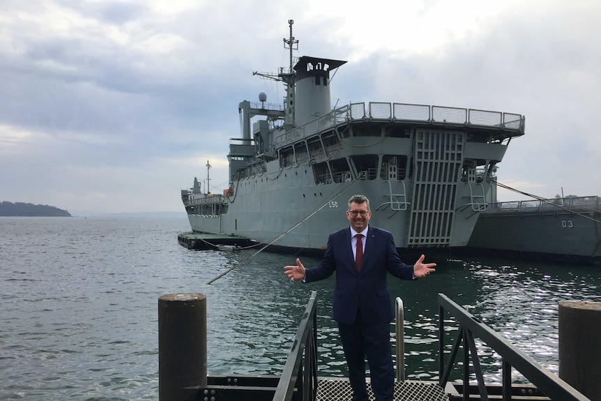 Member for Hinkler Keith Pitt stands in front of a large navy vessel.