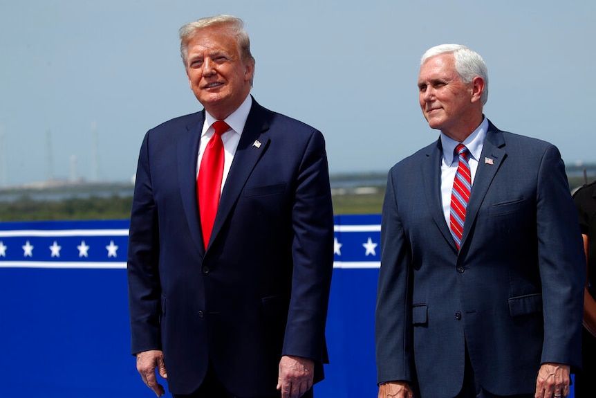 President Donald Trump stands with Vice President Mike Pence standing on a podium smiling.