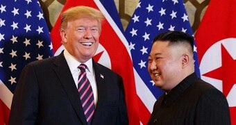 Donald Trump and Kim Jong-un laughing and smiling with a backdrop of US and North Korean flags.