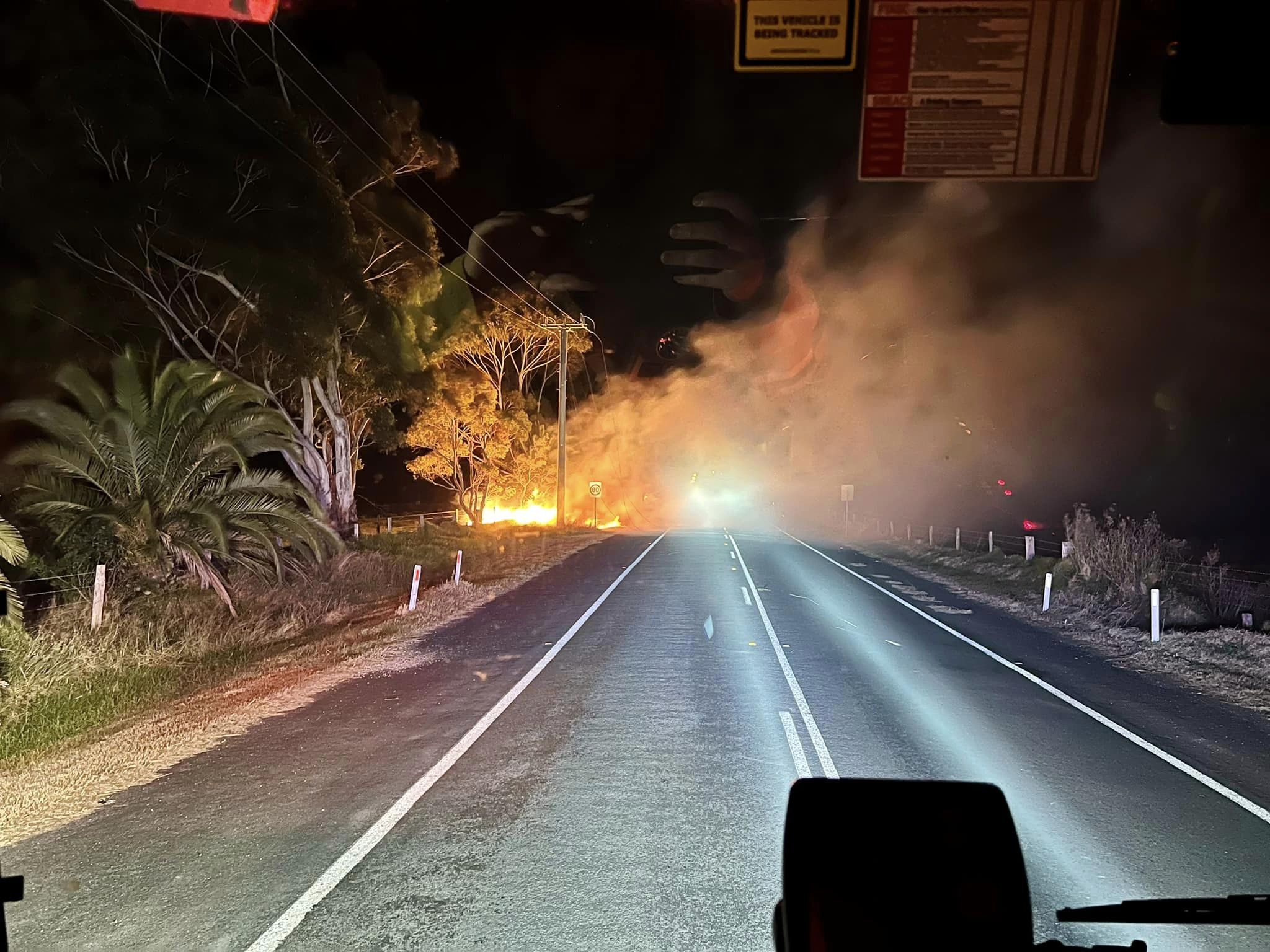 A fire breaks out on a road at night time, shot from inside a fire truck.