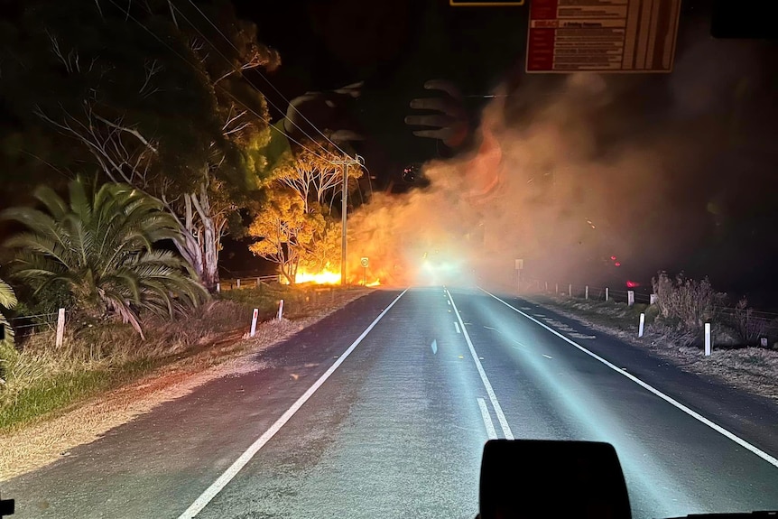 A fire breaks out on a road at night time, shot from inside a fire truck.