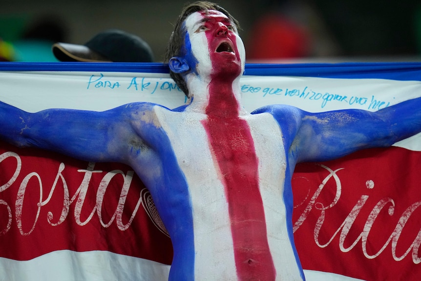 A fan painted in Costa Rica's colors holds up the country's flag at the Qatar World Cup.