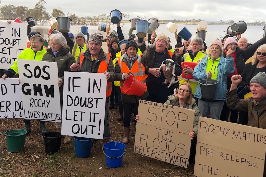 a group of people hold signs and buckets in front of a lake 