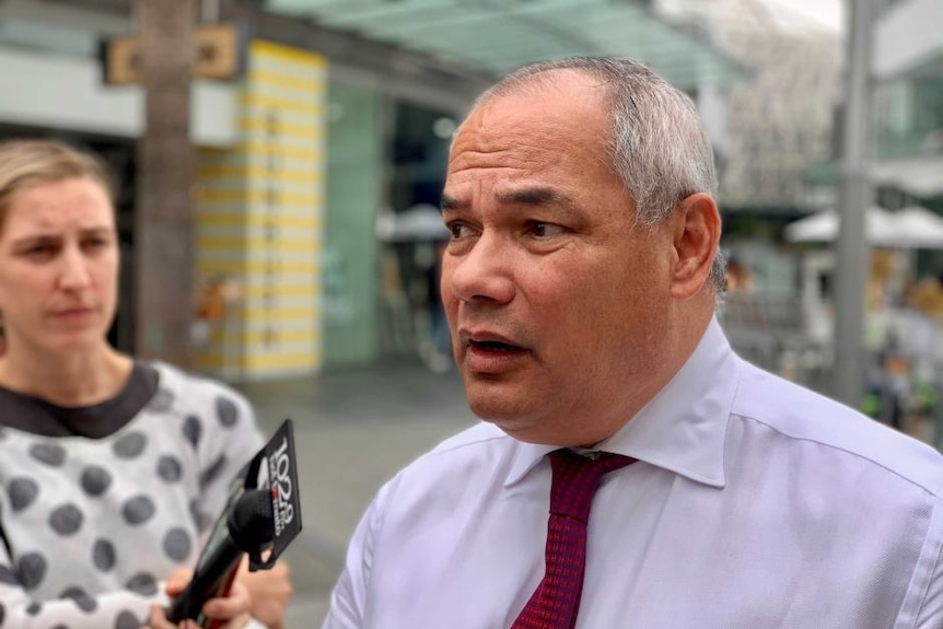 A man wearing a red tie talks to the media.