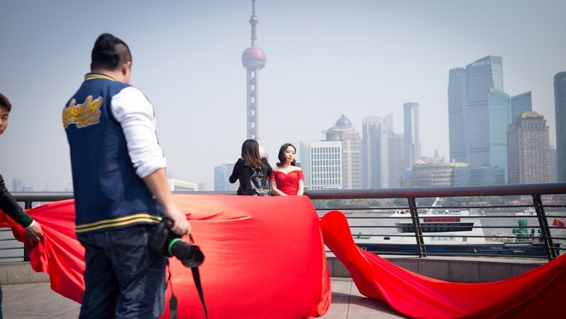 A woman wearing a red wedding dress poses for a photo in front of Shanghai's Oriental Pearl Tower.