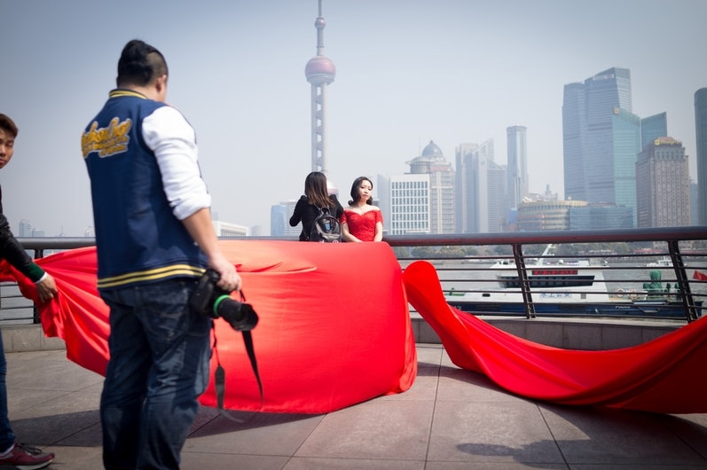 A woman wearing a red wedding dress poses for a photo in front of Shanghai's Oriental Pearl Tower.