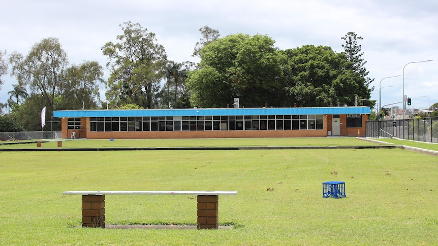 A bowling green with a long brick 1970s bowls club building