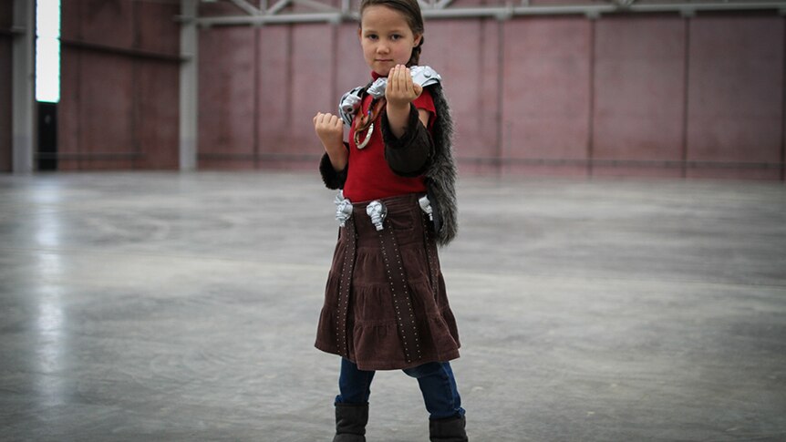 A young girl in leather skirt with skull detail at the belt, and skull-shaped clips holding on a fur cloak.