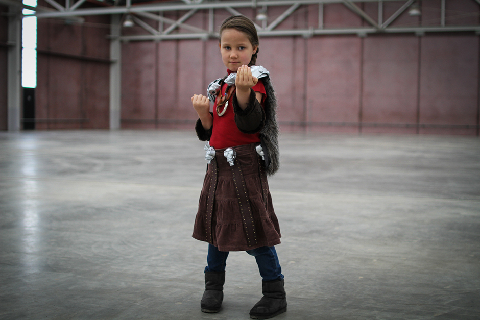 A young girl in leather skirt with skull detail at the belt, and skull-shaped clips holding on a fur cloak.