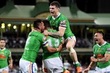 A Canberra Raiders NRL player jumps in the air as he embraces two teammates after a try was scored against the Sydney Roosters.