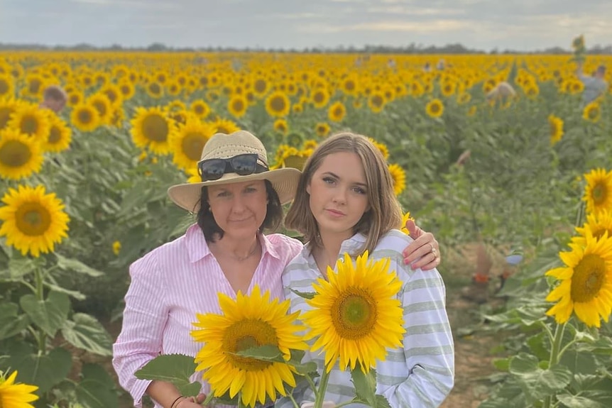 Woman standing in a field of sunflowers with her daughter Stella, 18