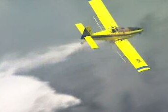 A plane drops a load of water over a smokey fire.