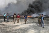 Tribal fighters walk as fire and smoke rises from oil wells set ablaze by Islamic State militants.