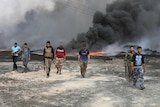 Tribal fighters walk as fire and smoke rises from oil wells set ablaze by Islamic State militants.