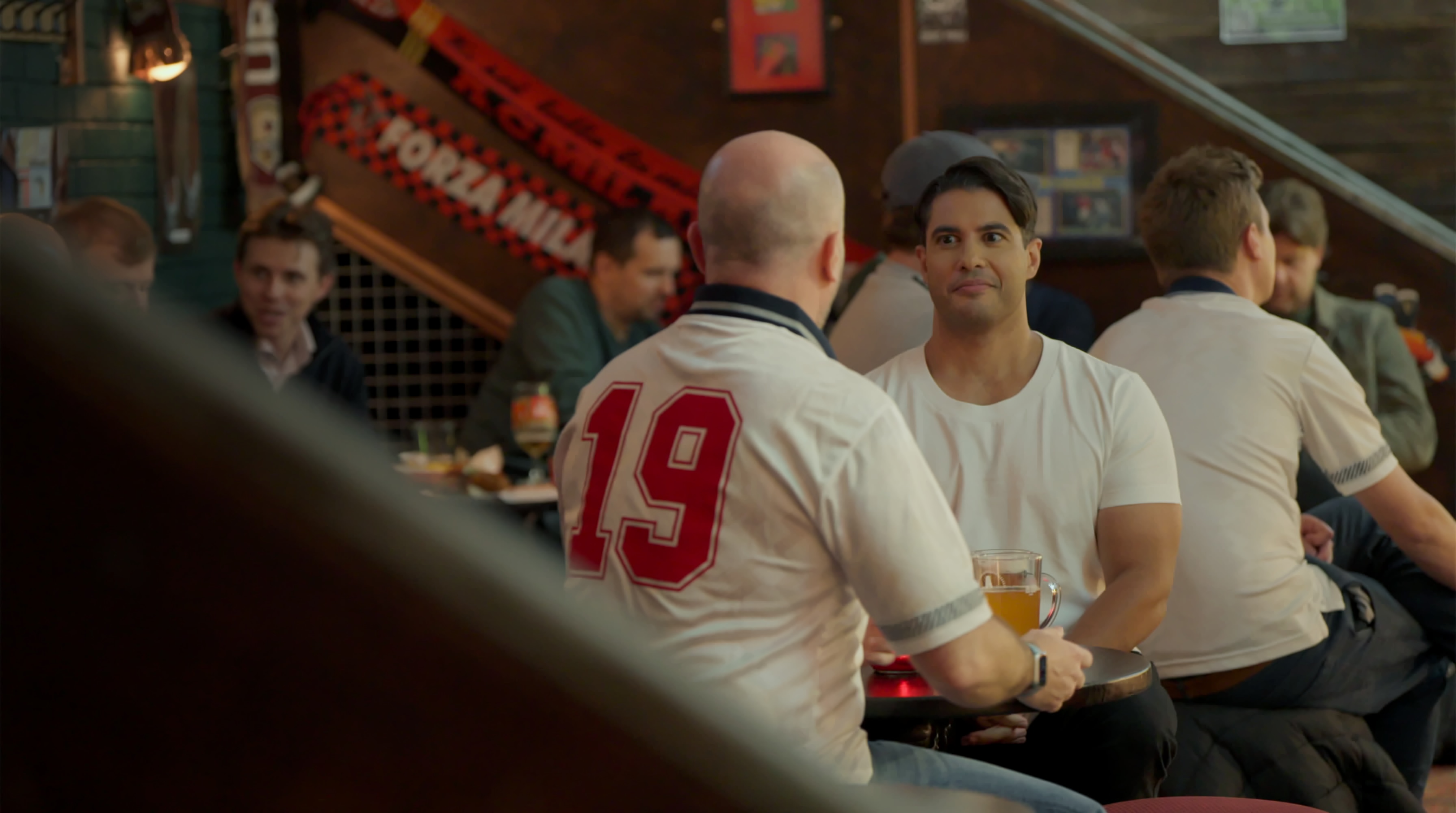Marc, right, sits with wide eyes next to a man at a bistro table at a pub while they share beers.