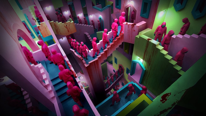 People in pink jumpsuits walk through a colourful labyrinth of staircases