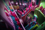 People in pink jumpsuits walk through a colourful labyrinth of staircases