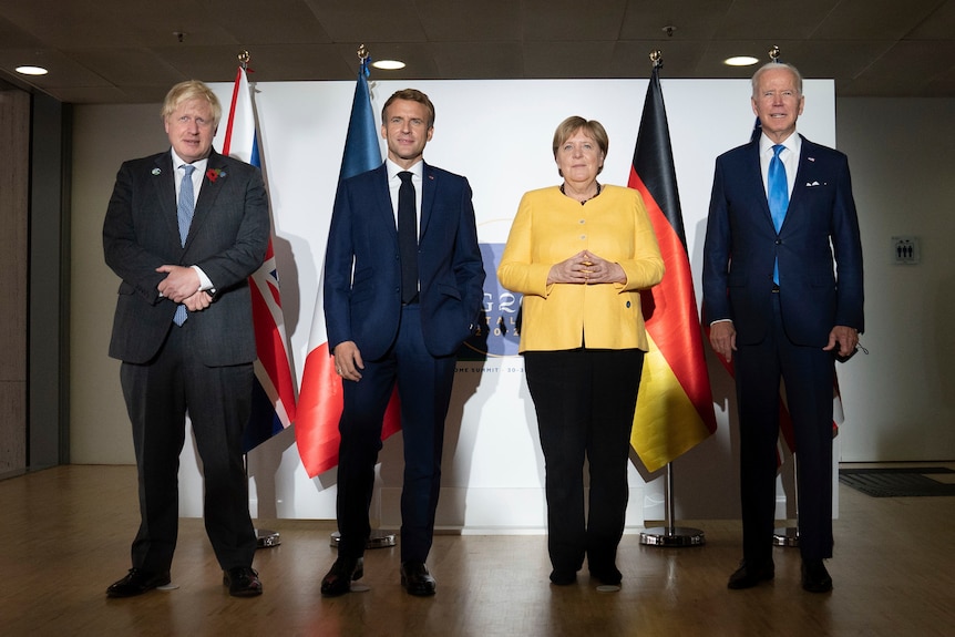 Three suited men and a woman in a yellow coat stand abreast for a photo in front of the flags of the countries they lead.