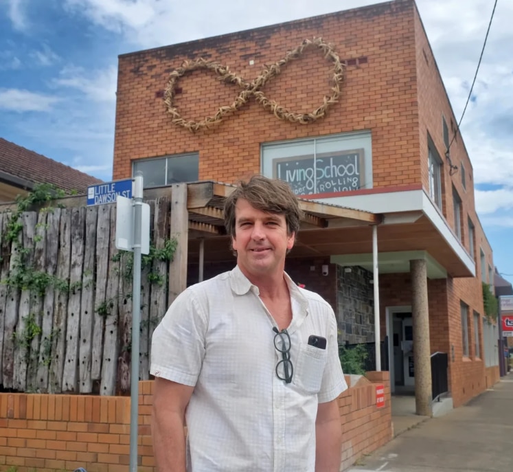 Un hombre se para frente a un edificio de ladrillo con un símbolo de infinito a un lado.