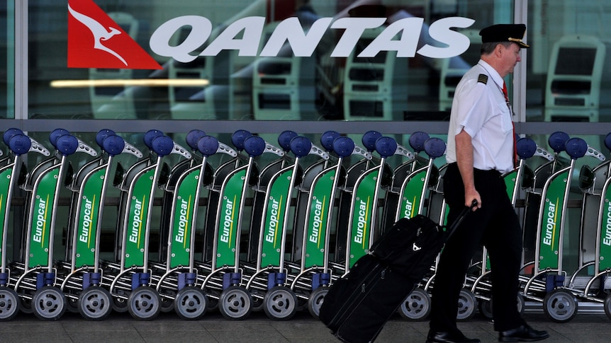 Pilot walks past Qantas sign at Sydney airport