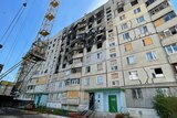 An apartment block with large blackened area from fire caused by a missile attack and a crane hovering above