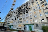 An apartment block with large blackened area from fire caused by a missile attack and a crane hovering above