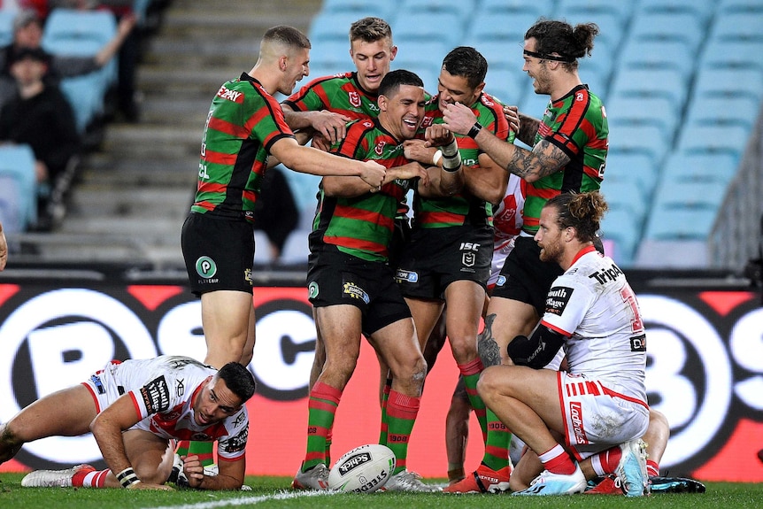 A group of male NRL players congratulate their teammate after he scored a try.