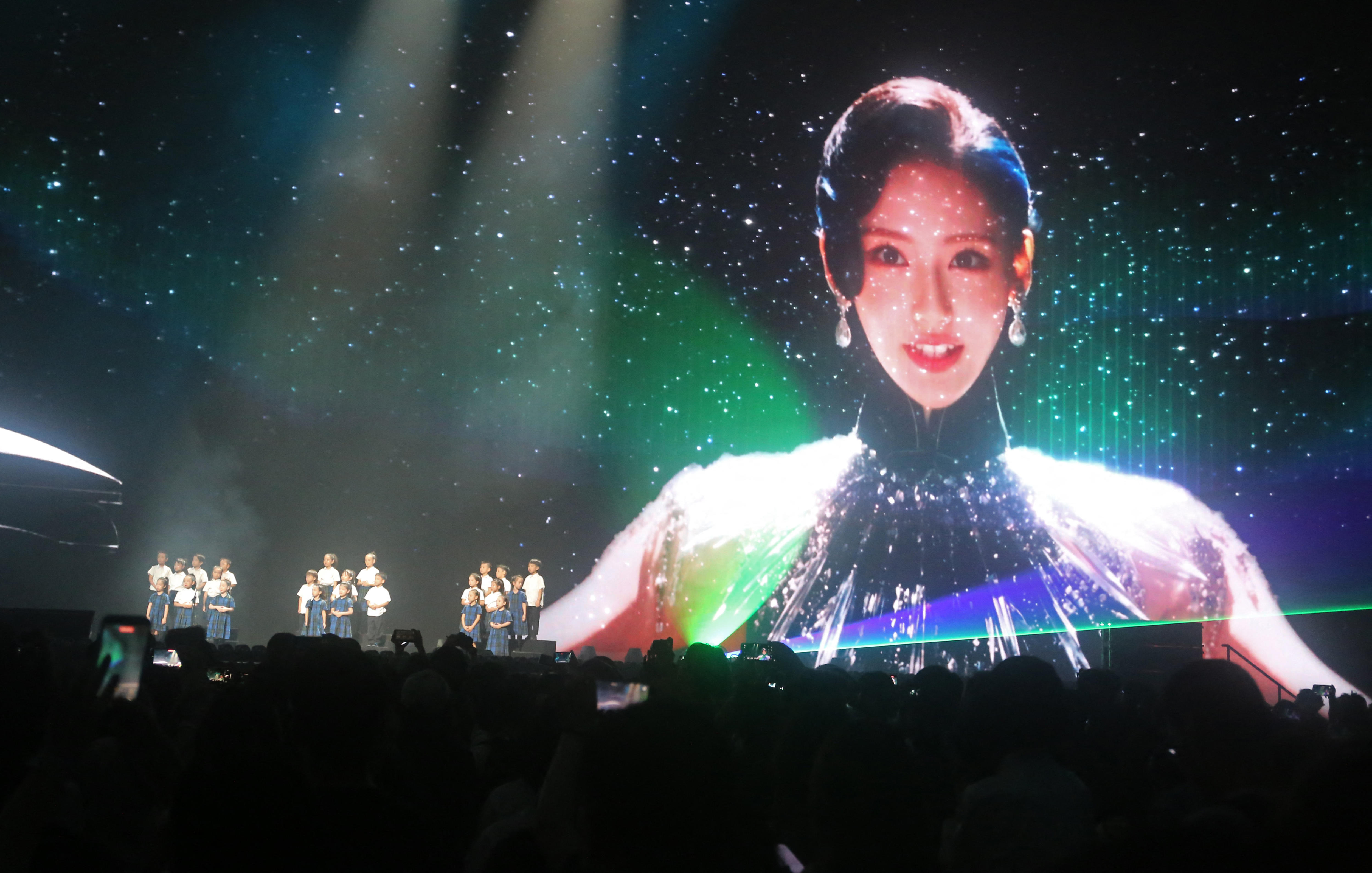 The image of a woman wearing large earrings and a black dress appears on a large screen behind a stage.