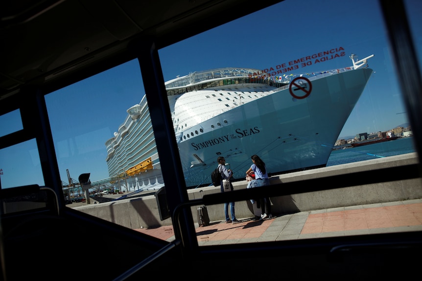 A large cruise ship, Symphony of the Seas, is seen through a window while docked