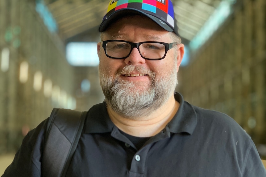 A man wearing a hat and glasses and holding a smartphone with a lens attached