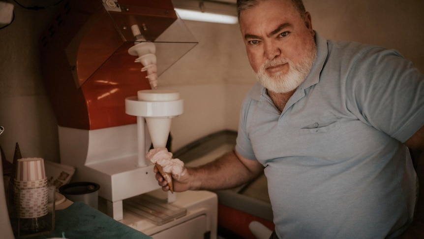 Man with grey hair and beard trying to look in a provocative, sexy way while holding an ice-cream in an ice-cream van