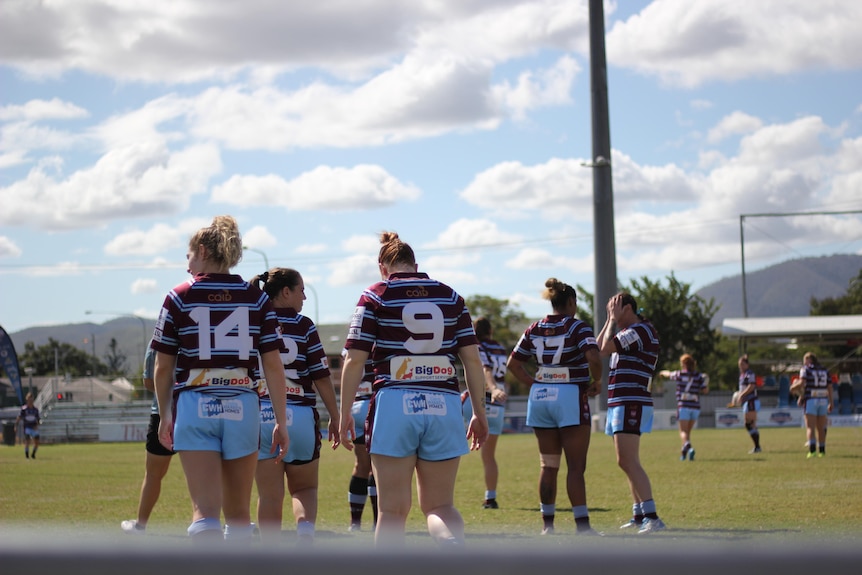 A group of women in maroon and blue jerseys walk onto a rugby pitch.