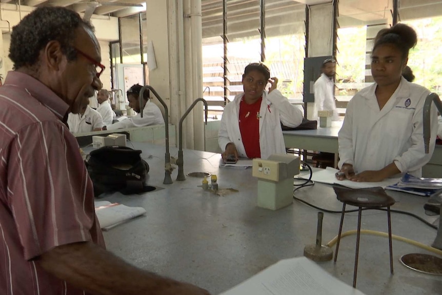 Professor Topul Rali speaks to two two students, who are wearing lab coats.