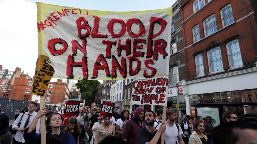 A large crowd carry banners and signs reading "Blood on their hands" walk outside Kensington Town Hall during protests.