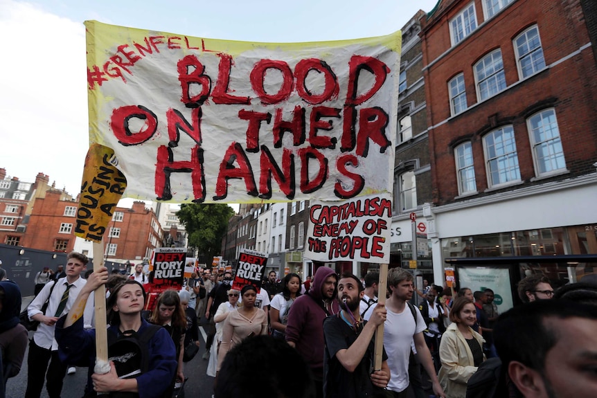 A large crowd carry banners and signs reading "Blood on their hands" walk outside Kensington Town Hall during protests.