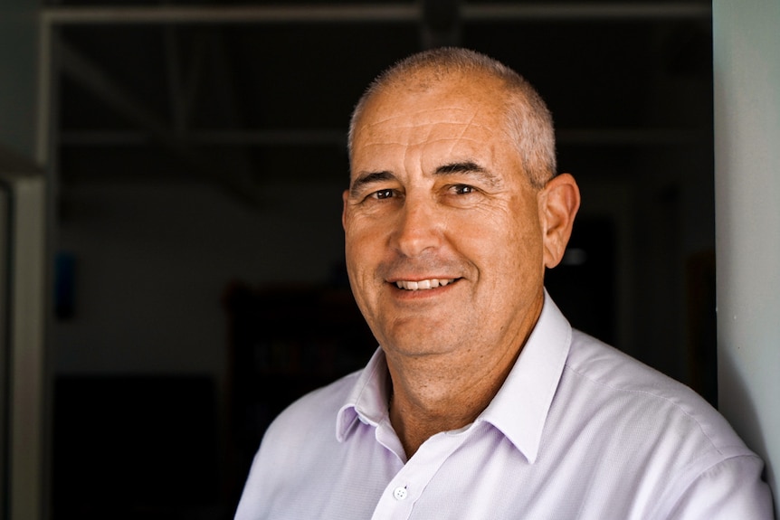 Close head shot of man standing in door frame with contrasting background wearing a white collard shirt