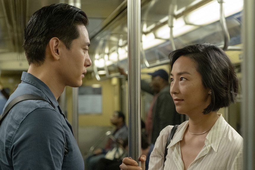 A Korean man with short dark hair, in a navy shirt, and a Korean woman with dark bob, in a white shirt, are in a subway carriage