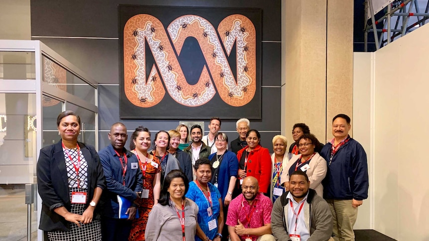 A group of men and women stand and crouch in front of the ABC indigenous designed sign