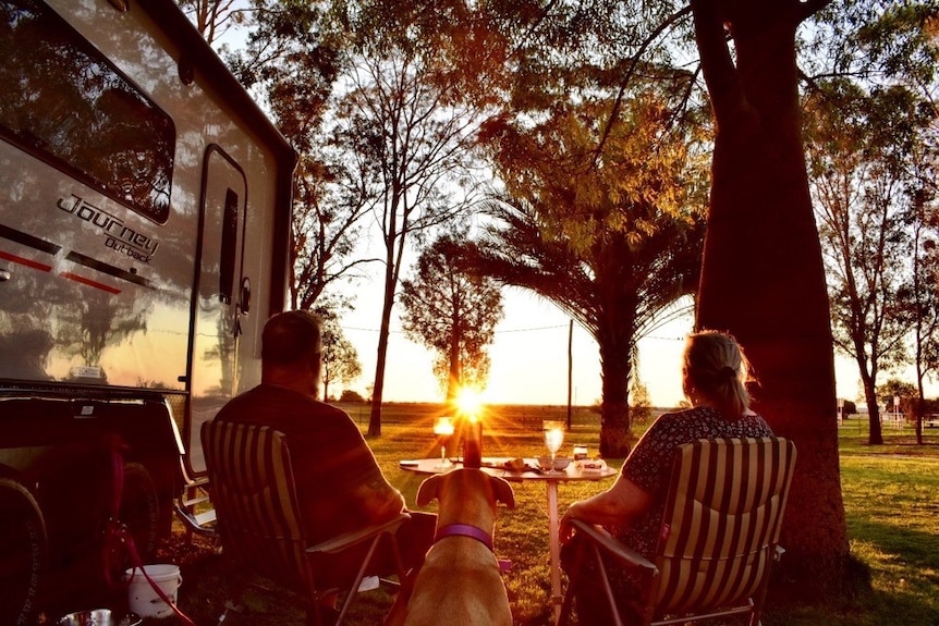 The backs of man and a woman next to their caravan watching the sun set